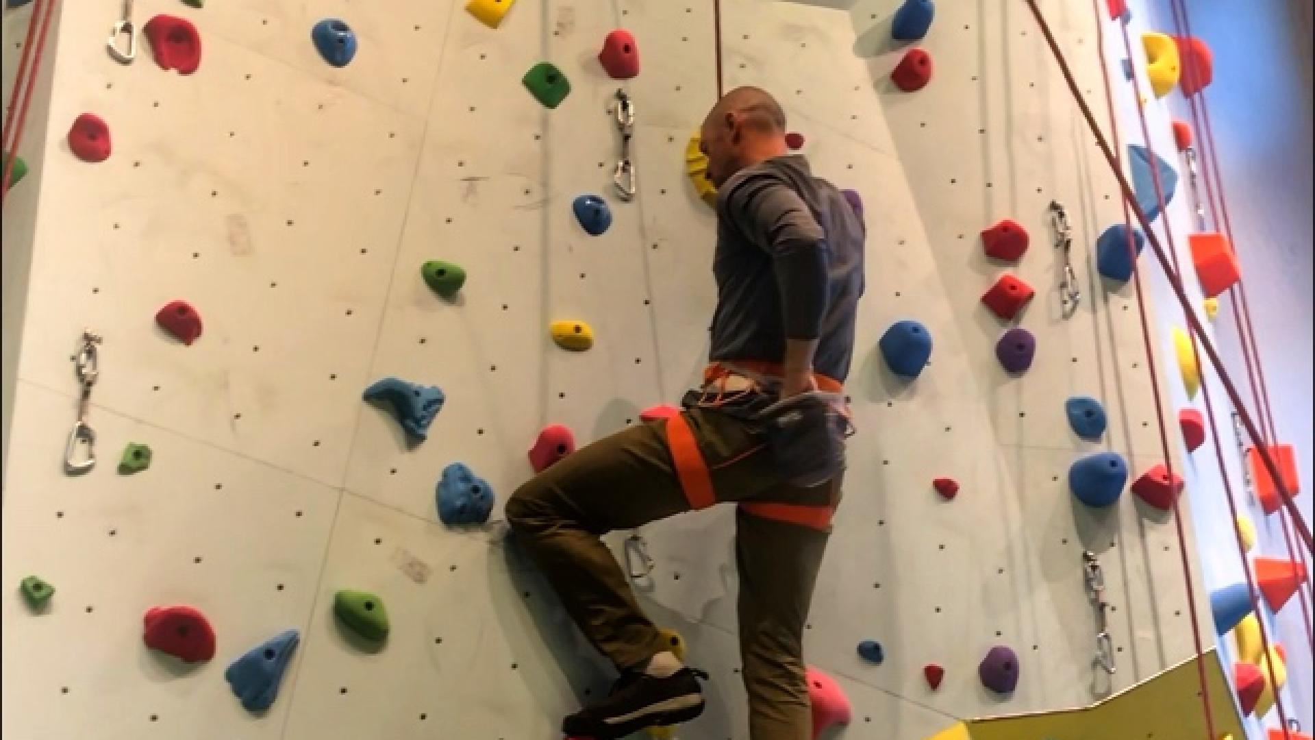 Climber scaling an indoor rock wall with colorful holds.